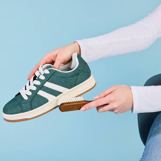 Person reinigt Sneaker-Schuh mit Schuhbürste