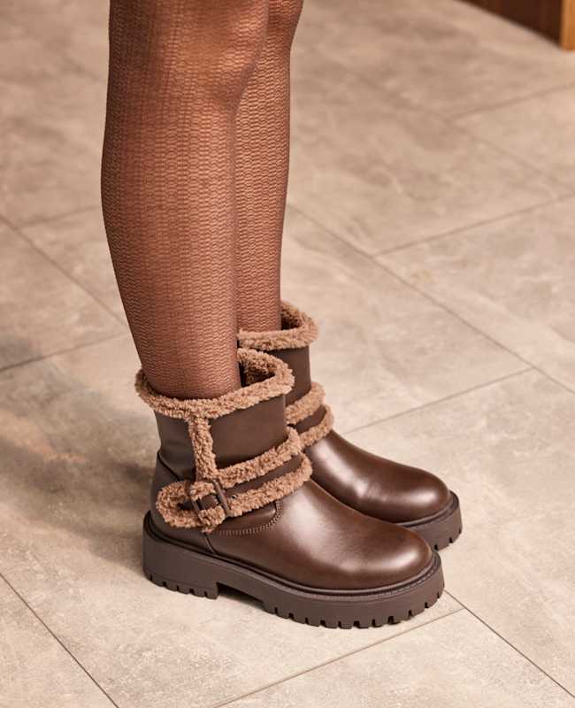 Frau trägt braune Stiefel mit Fell-Applikationen, steht auf Fliesenboden
