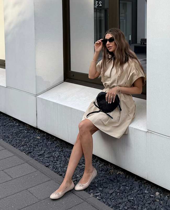 Frau in beigem Kleid im Casual Look, kombiniert mit schwarzer Handtasche und silbernen Ballerinas