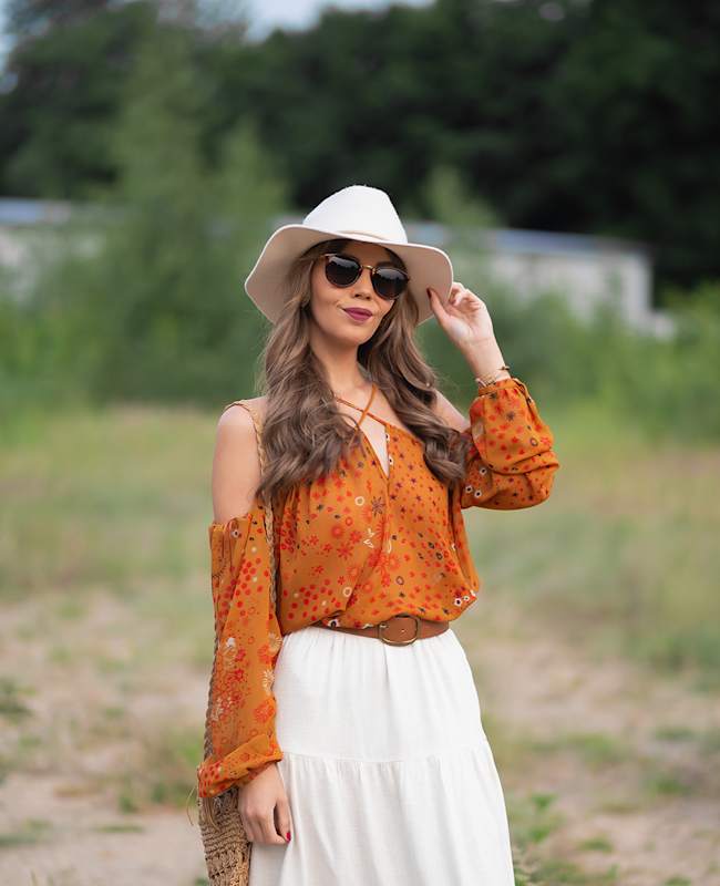 Frau in lockerem Festival-Outfit im Coachella Style, bestehend aus Maxirock, Bluse und weißem Hut