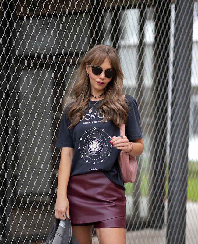 Frau mit Sonnenbrille und rockigem Outfit, stehend vor Gitterzaun