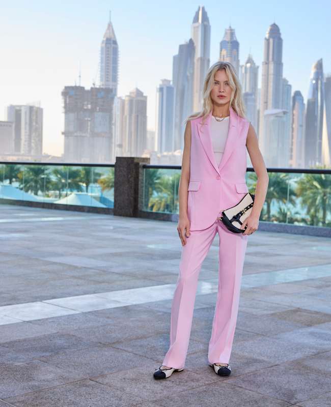 Frau in pinkem Office-Suit, mit passender Handtasche, stehend vor Dubais Skyline