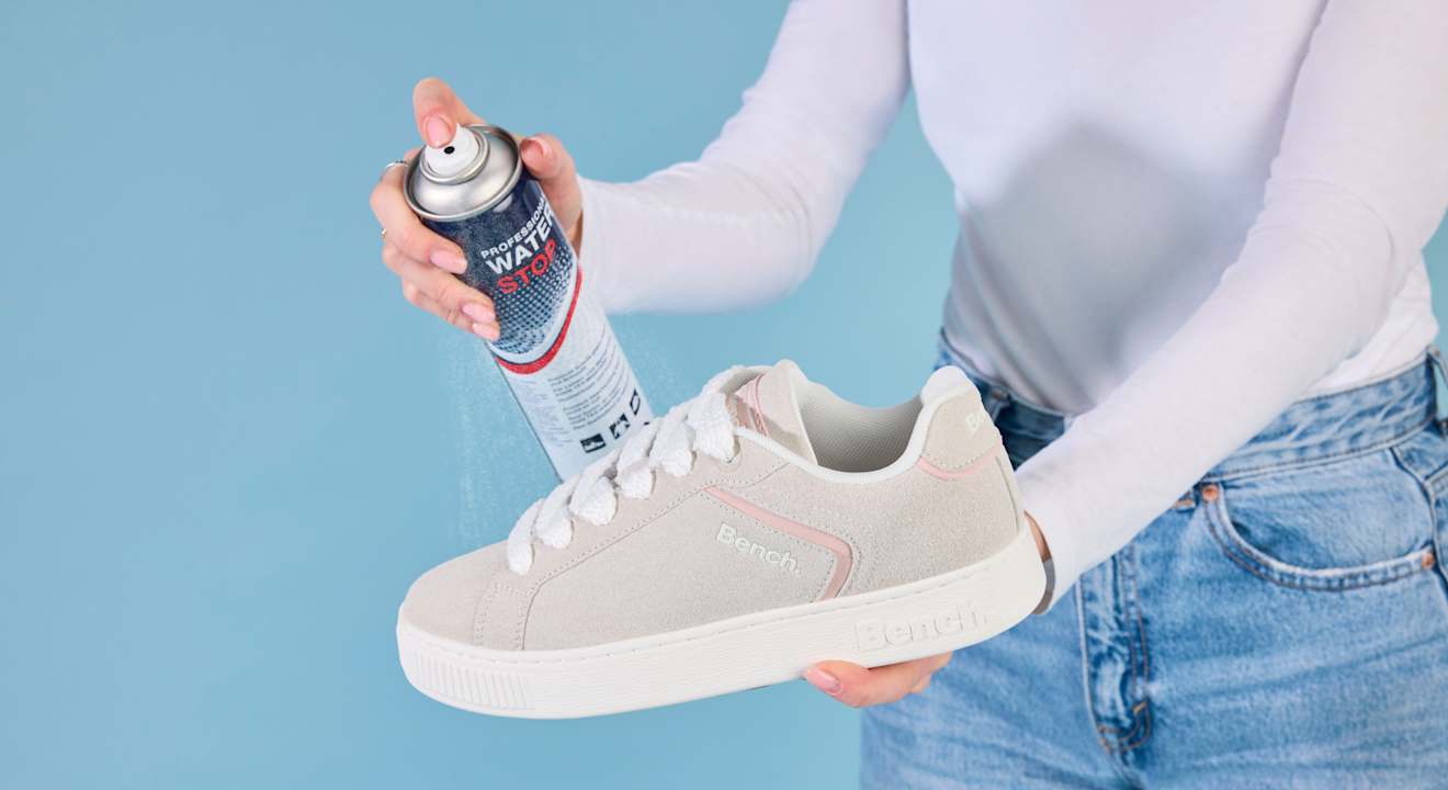 Frau hält weißen Sneaker-Schuh und sprüht diesen mit Imprägnierspray ein