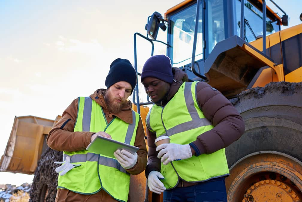 Two construction workers in front of wheel loader looking at tablet