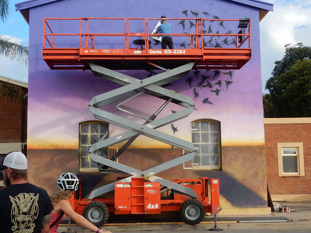 man on a rough terrain scissor lift painting a mural