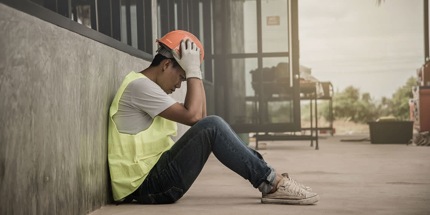 Man sitting on concrete ground with head in hands.