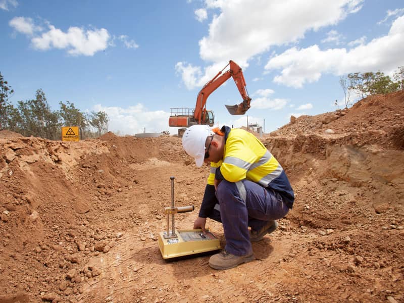 Worker on job site, excavator in the background.