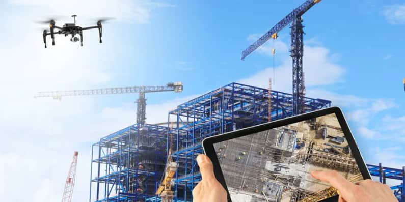 A drone with a camera flying over a construction site with a person holding a tablet that shows the camera view