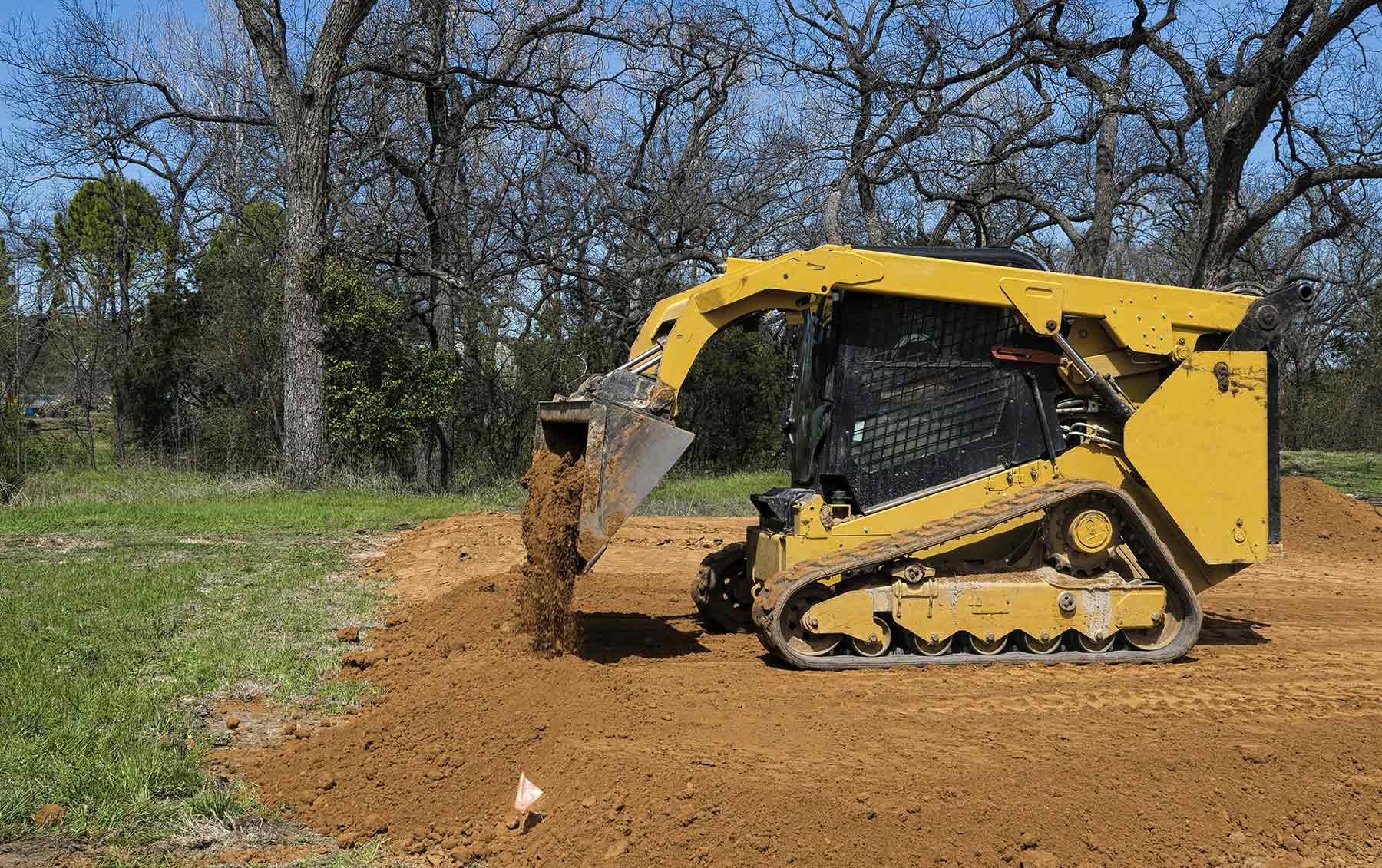 Skid steer dumping and levelling dirt by grass