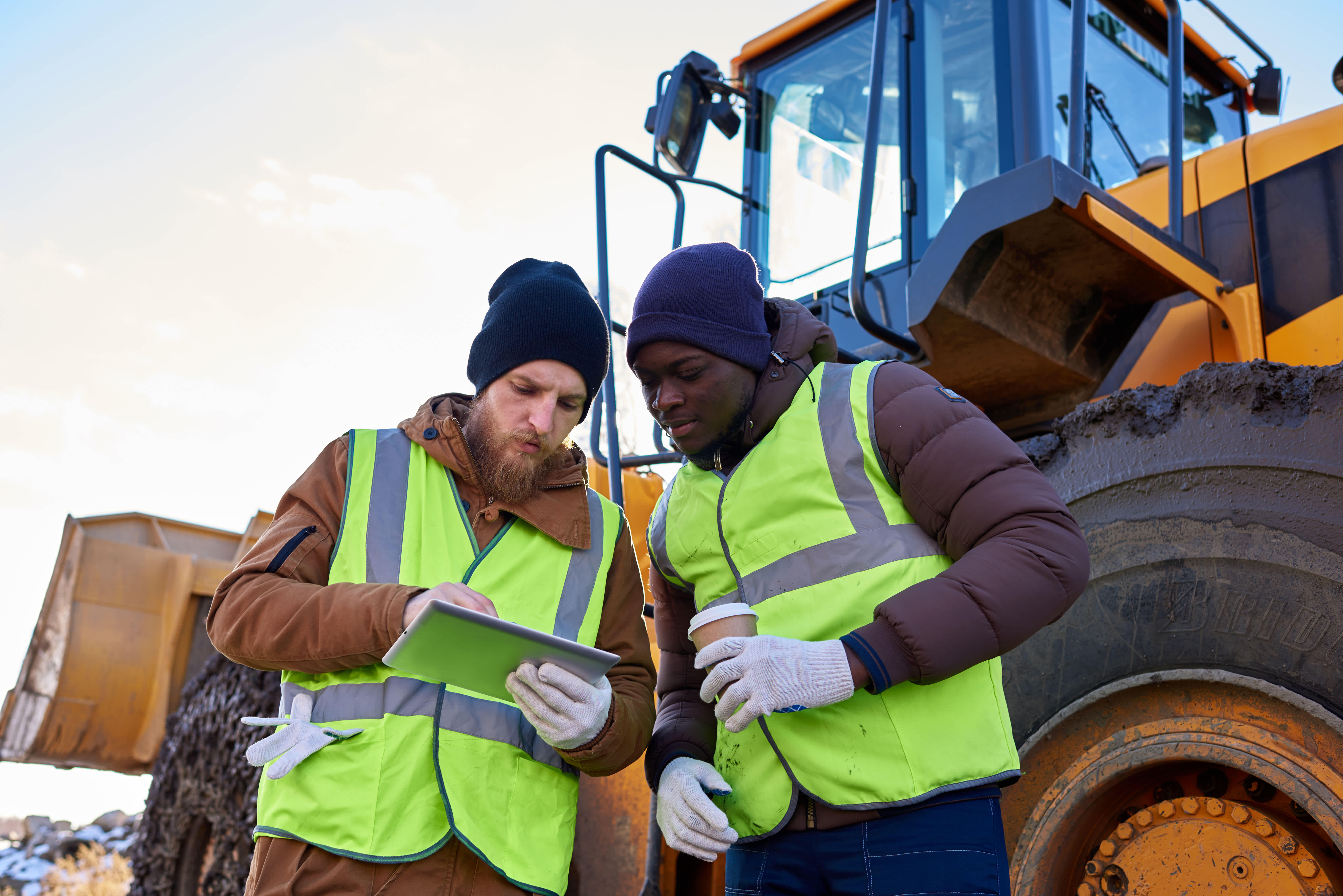 two construction workers standing in front of wheel loader looking at tablet