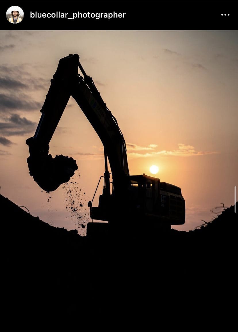 excavator hauling dirt back lit by a sunset