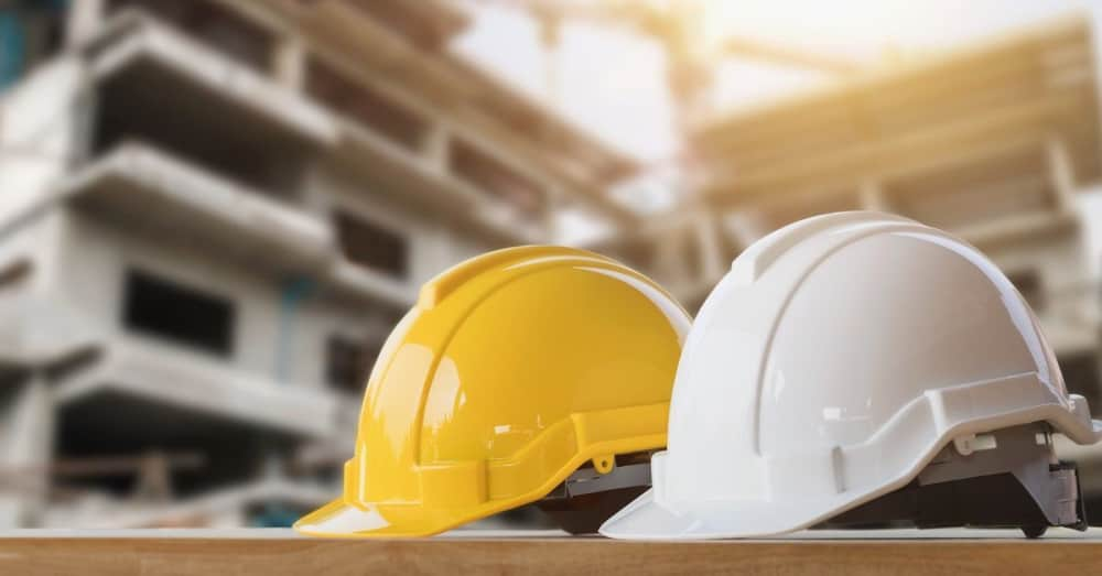 Two hard hats, one yellow, one white, sitting on a table in front of a building. 