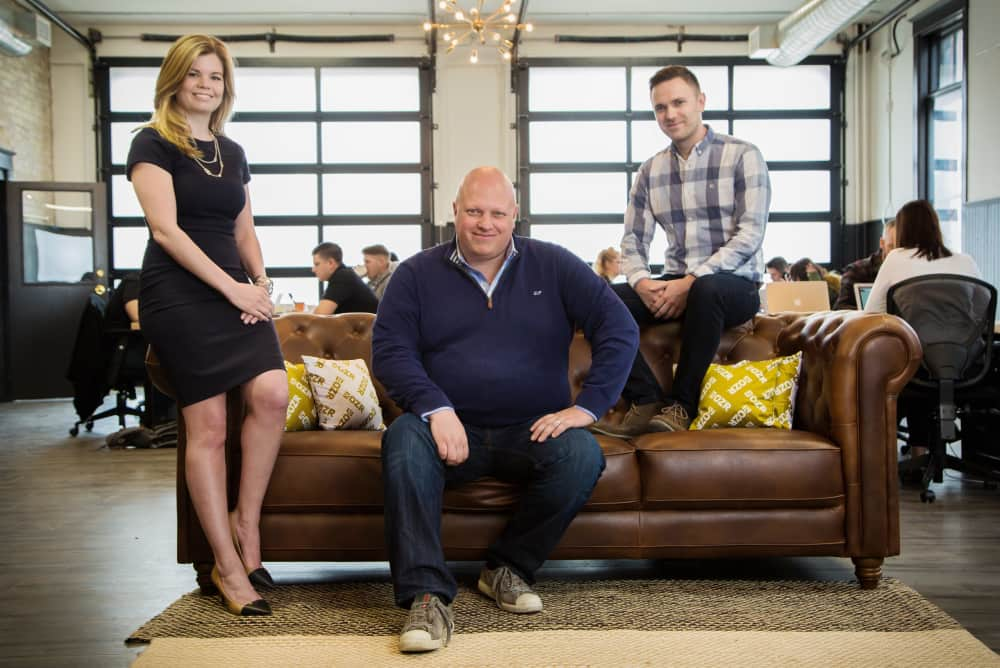 DOZR co-founders, Kevin, Erin and Tim, sitting on a brown couch in the DOZR office.