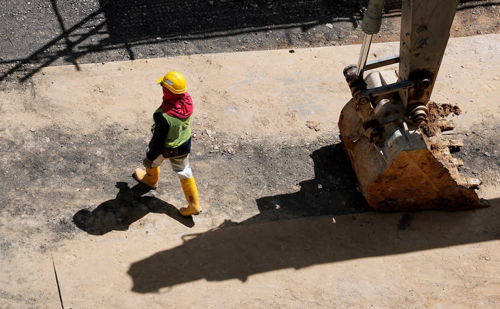 Construction worker walking on construction site near excavator bucket