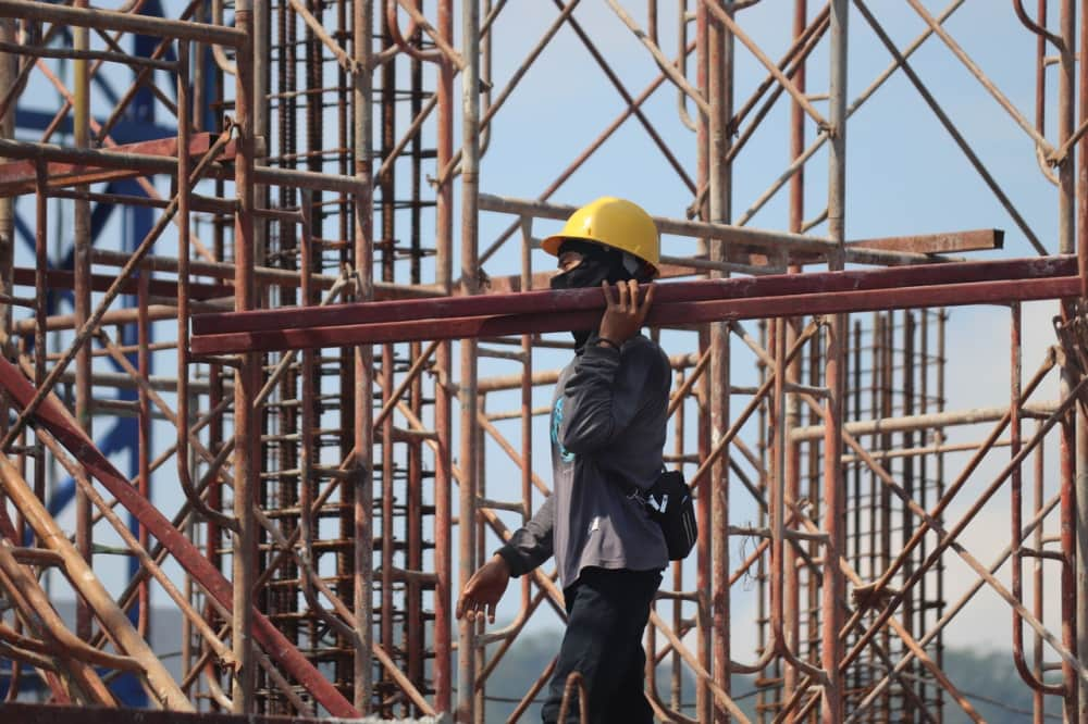 Construction worker walking carrying material in front of scaffolding