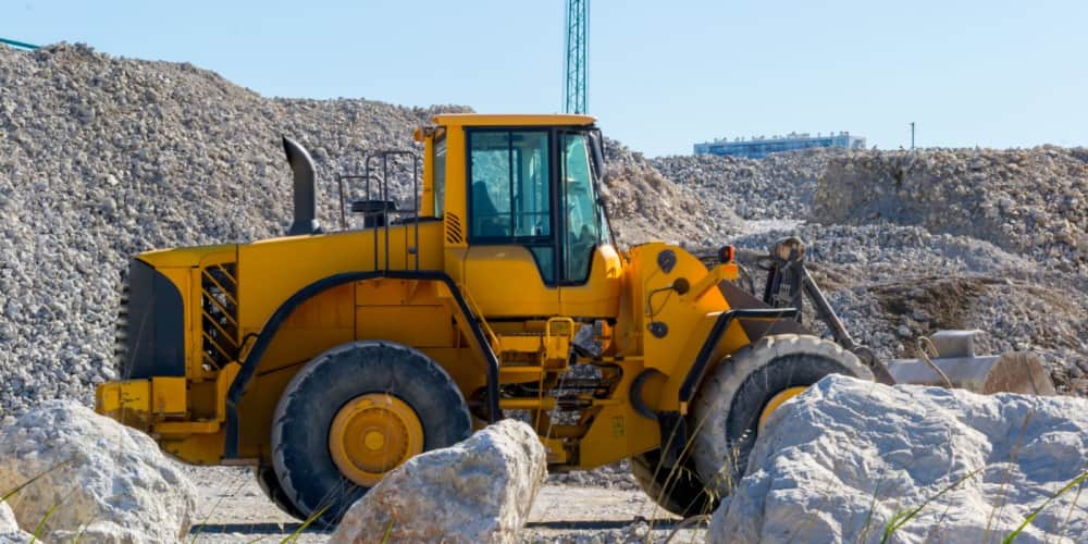 Yellow wheel loader sitting idle with big boulders in front of it and small rocks behind it