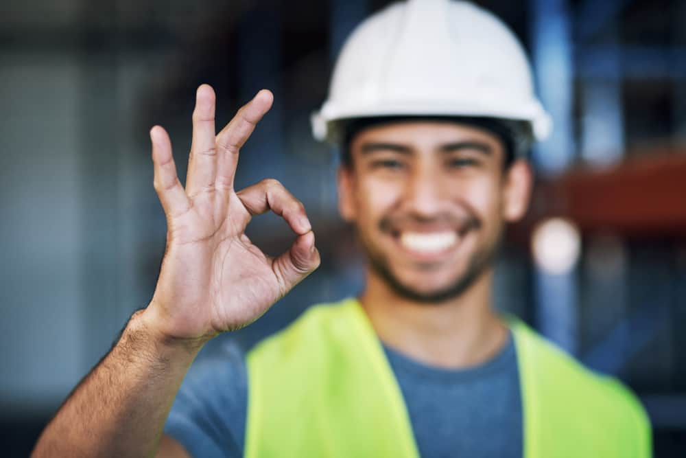 Equipment operator with ear protection, workwear, and hard hat climbing into his equipment