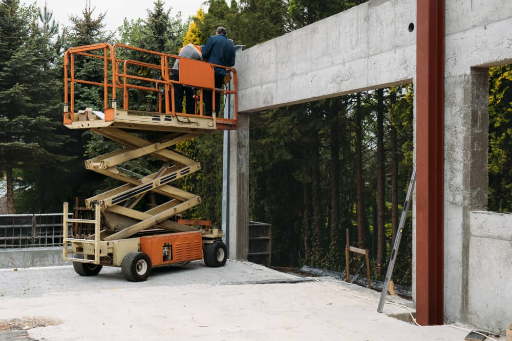 Scissor lift with two people on it doing work on concrete