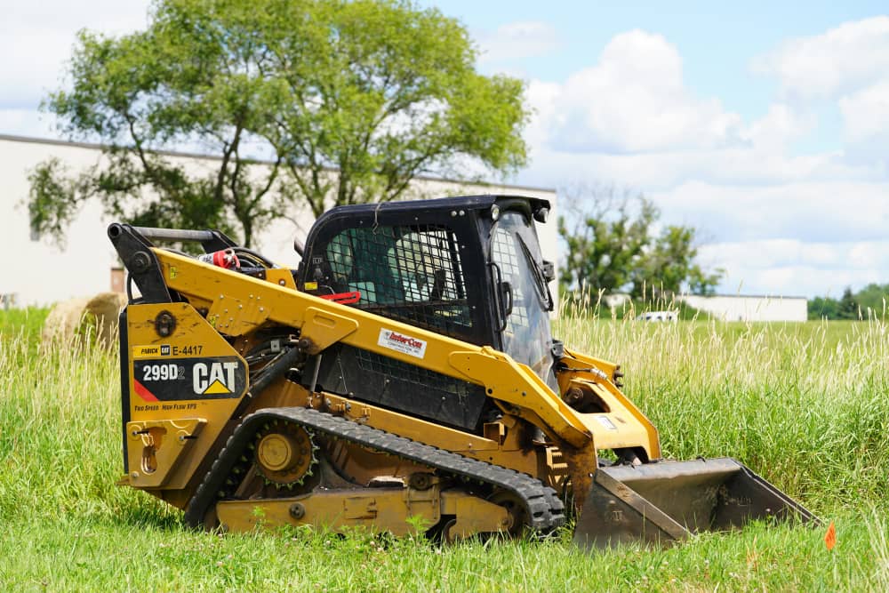 CAT 299D compact track loader with a bucket attachment in a grass field