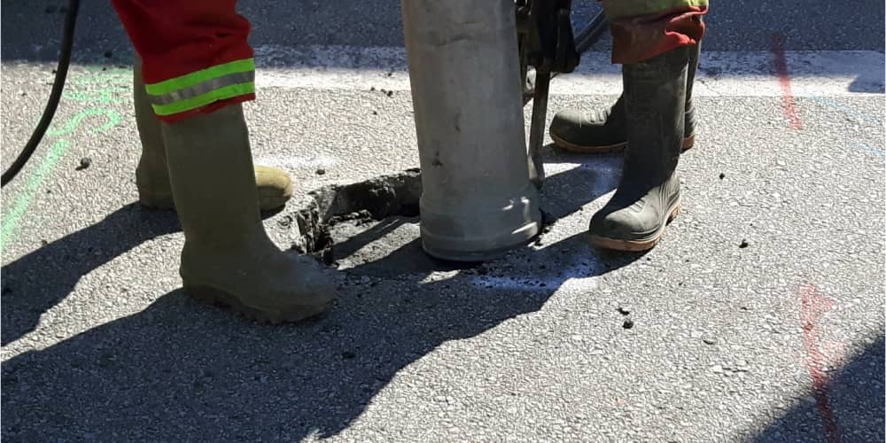 Two workers performing vacuum excavation on asphalt