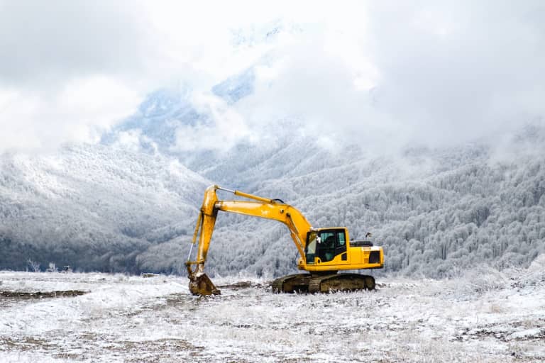 rented excavator parked in snowy field in front of mountain 