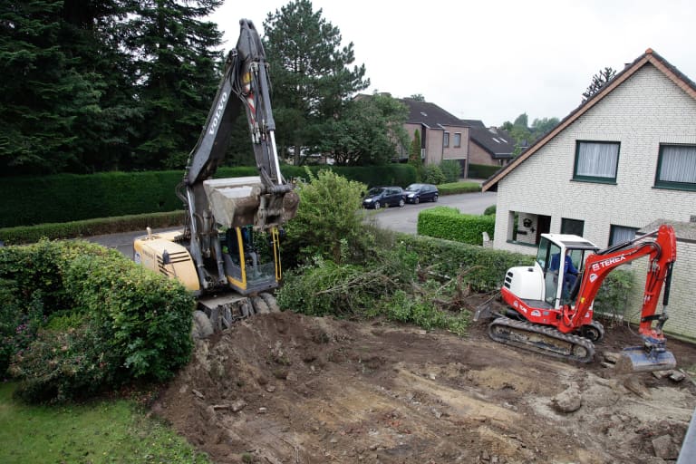 Two excavators working on a yard by a house