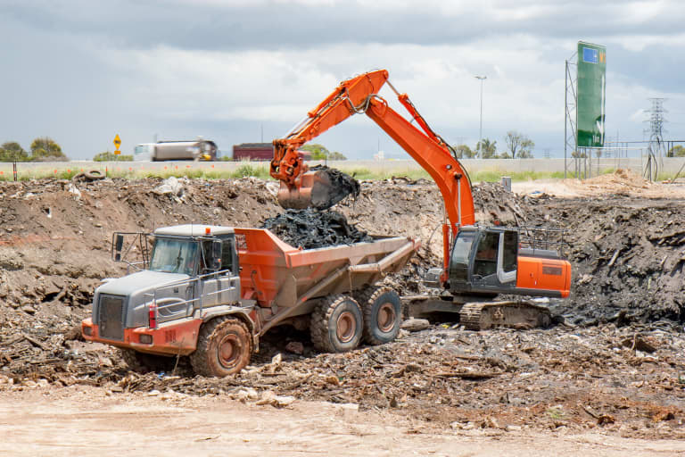 Backhoe digging dirt and dumping it into back of dump truck