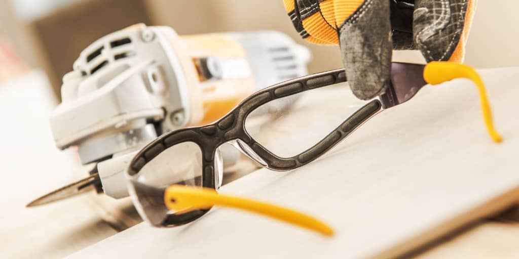 Safety glasses and power equipment on a desk with a hand reaching for them