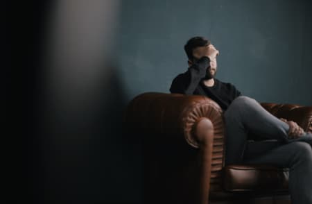 Young man holding his head, sitting in a chair. 