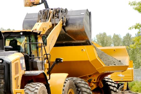 Backhoe loader dumping dirt into an articulating dump truck