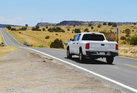 White construction pick up truck driving down a road