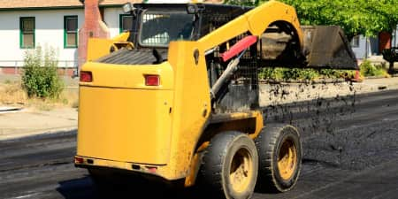 Yellow skid steer dumping asphalt on a paving job