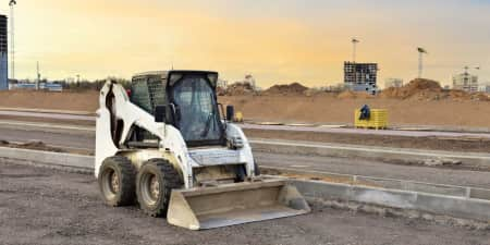 White skid steer with a cab idle on a road work project