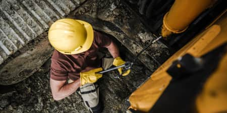 Equipment operator with a yellow hard hat and gloves greasing an excavator