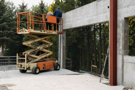 Scissor lift with two people on it doing work on concrete