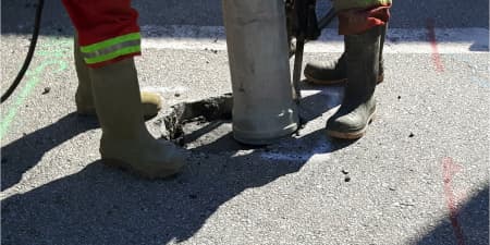 Two workers performing vacuum excavation on asphalt