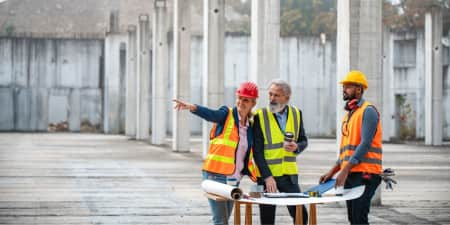 Three contractors on a job site looking at building plans