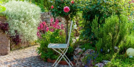 Backyard garden with a chair, stone path, and lots of annuals and perennials