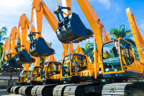 Lineup of excavator rentals with palm trees and blue sky in background