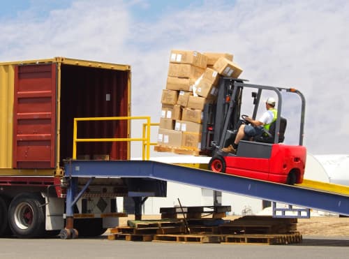 Forklift unloading pallet of materials from truck on construction site