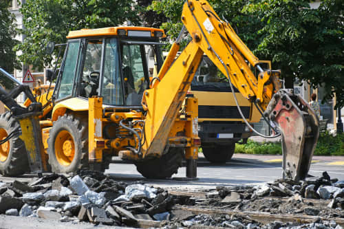 Backhoe with hammer attachment breaking road