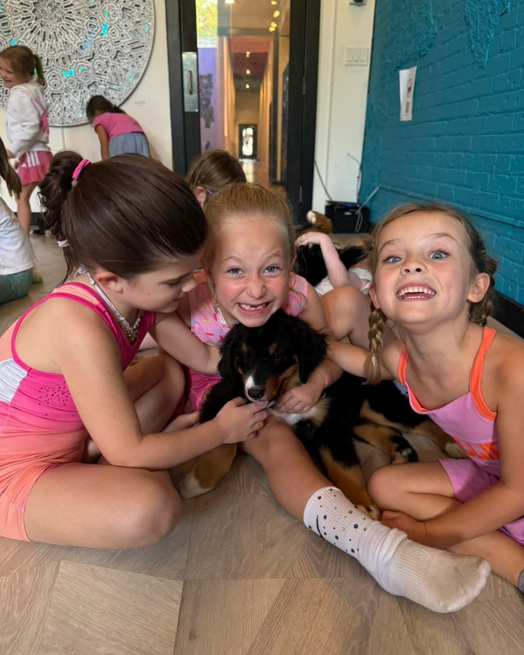 Kids smiling with Bernese Mountain Dog puppies during a birthday party at Downward Dog Puppy Yoga
