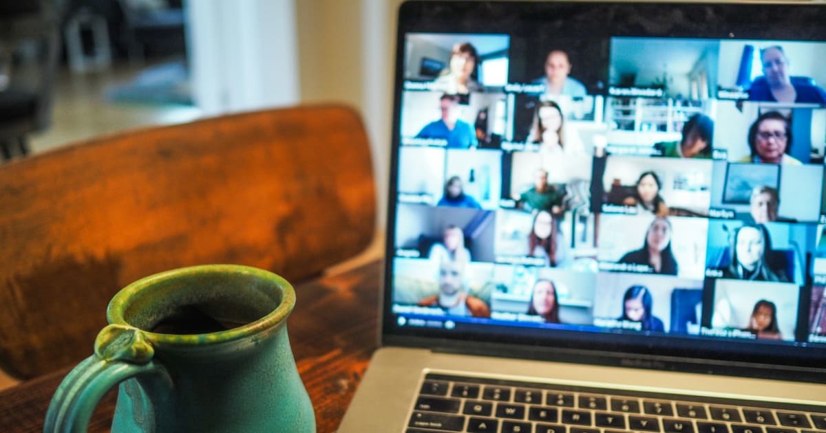 A ceramic mug beside an open laptop showing a grid video call in progress