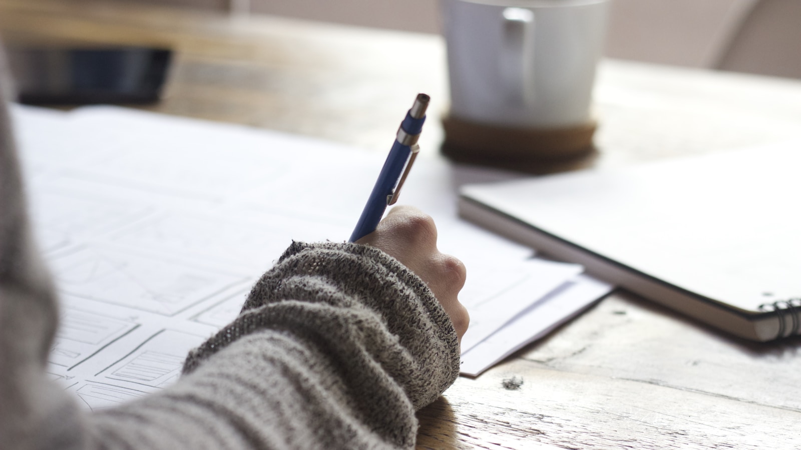 Person writing notes at a desk with a laptop