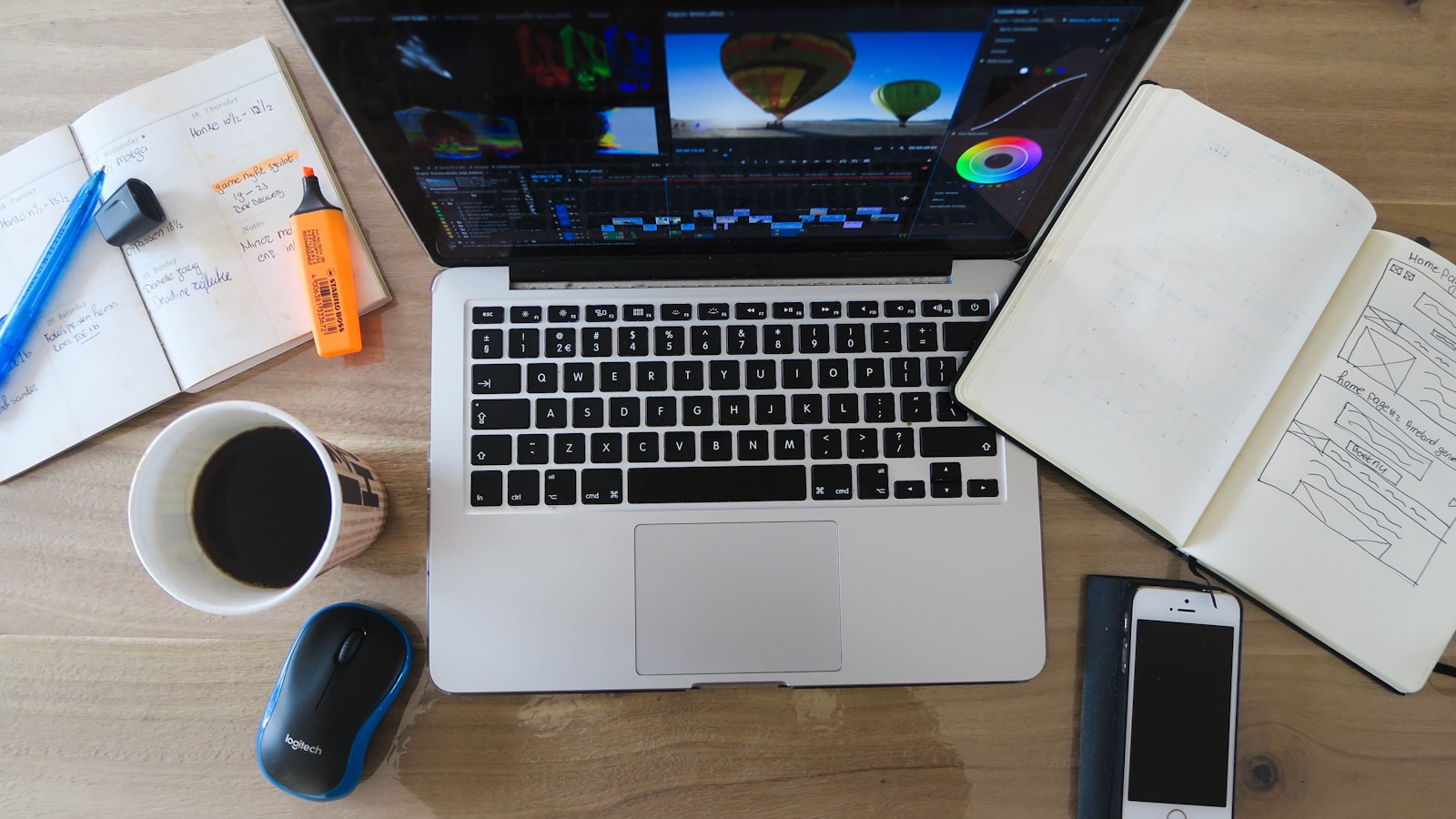Laptop, notebooks, phone, and coffee arranged on a working desk