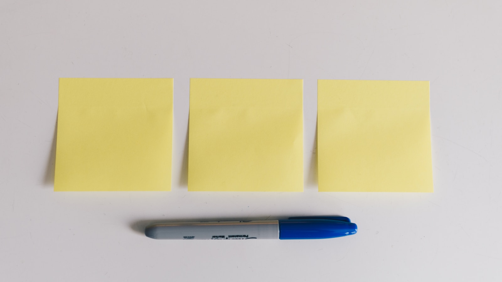 Three yellow sticky notes and a pen on a white surface