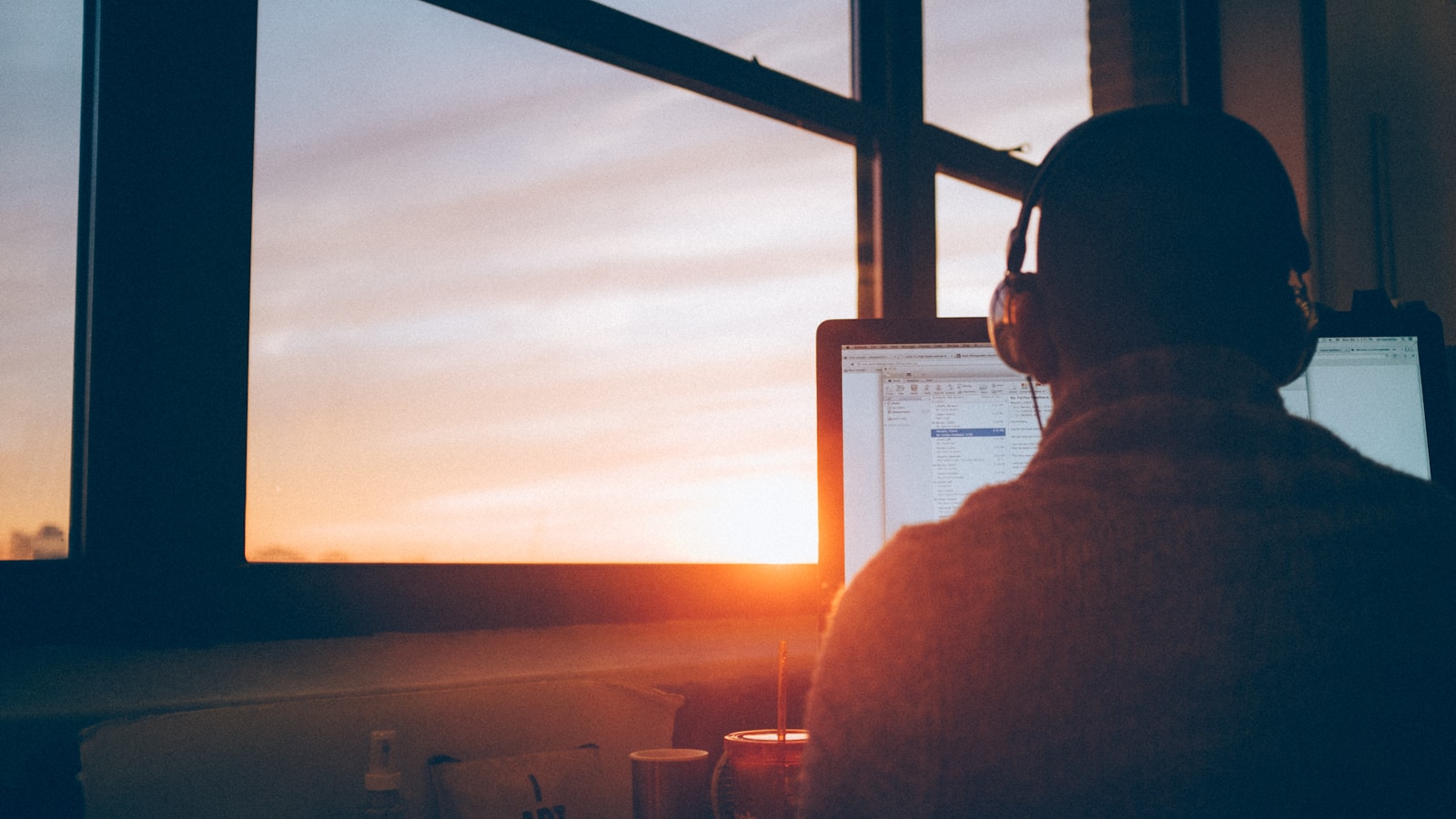 Person working at a multi-monitor desk near sunset