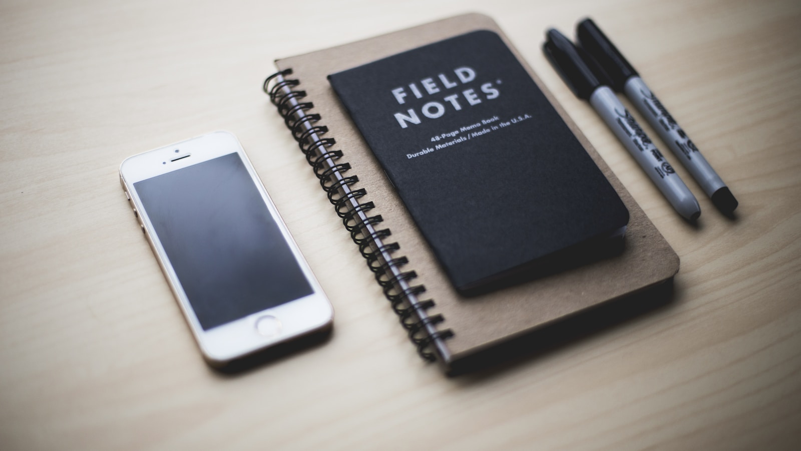 Field Notes notebook, phone, and pens on a table