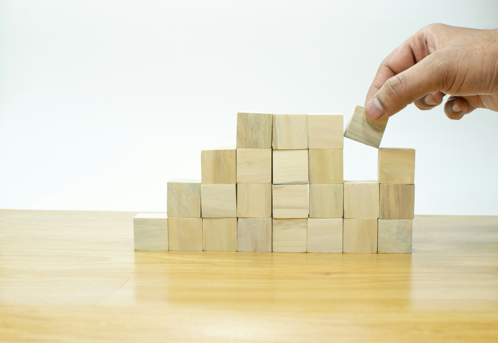 A hand placing a wooden block onto a structure of stacked blocks, representing a website built block by block