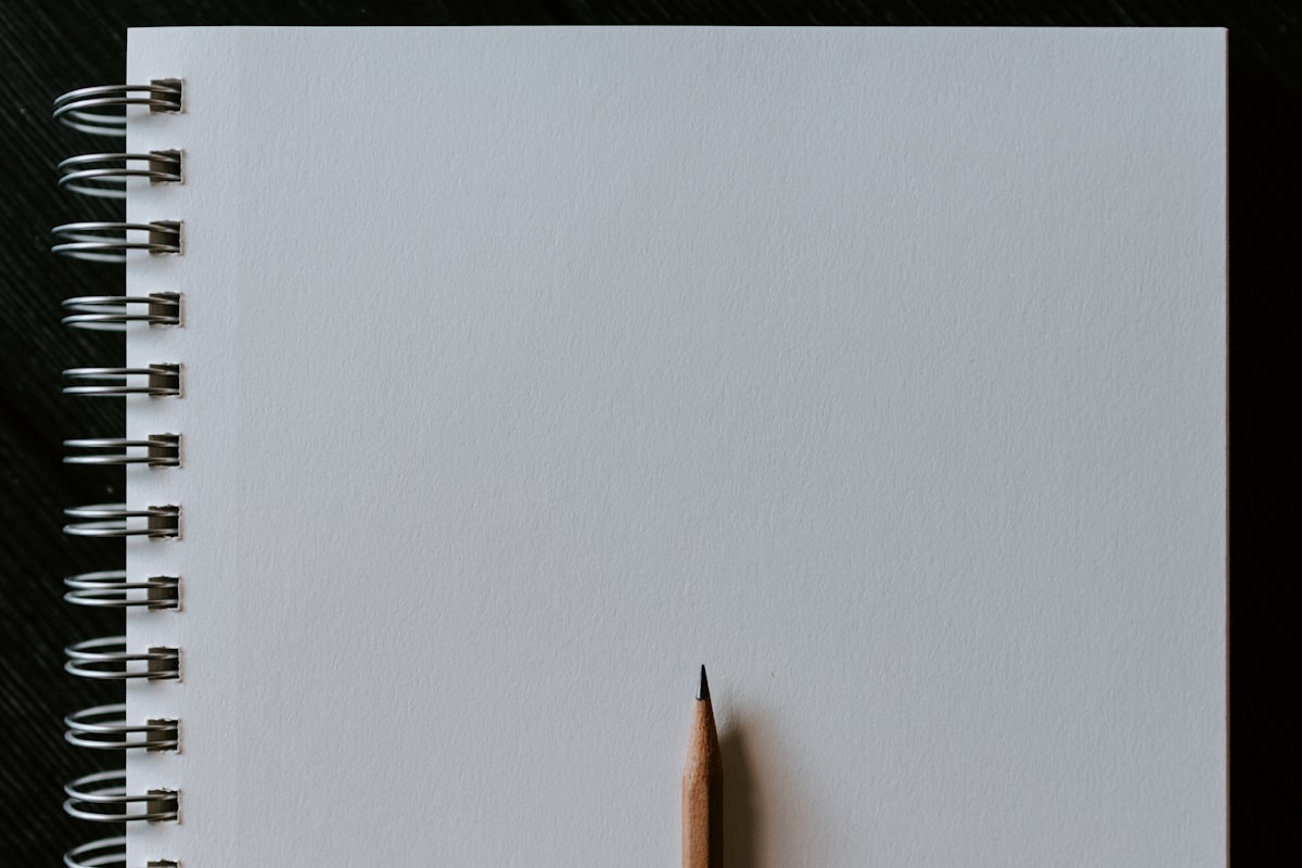 A blank spiral notebook with a sharpened pencil resting on the open page against a dark background